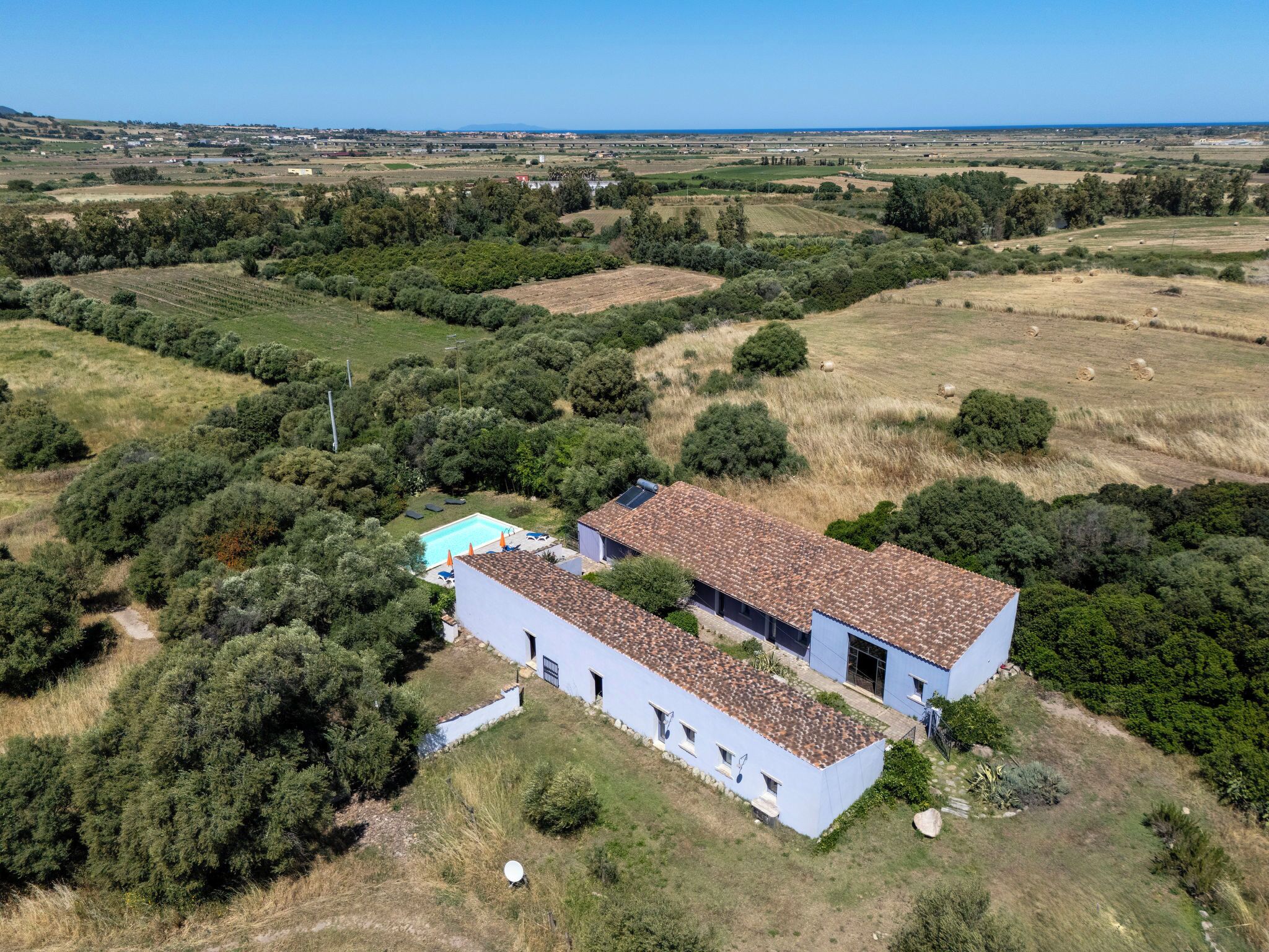 Una casa de un piso con techo de tejas, rodeada de un jardín y campos.