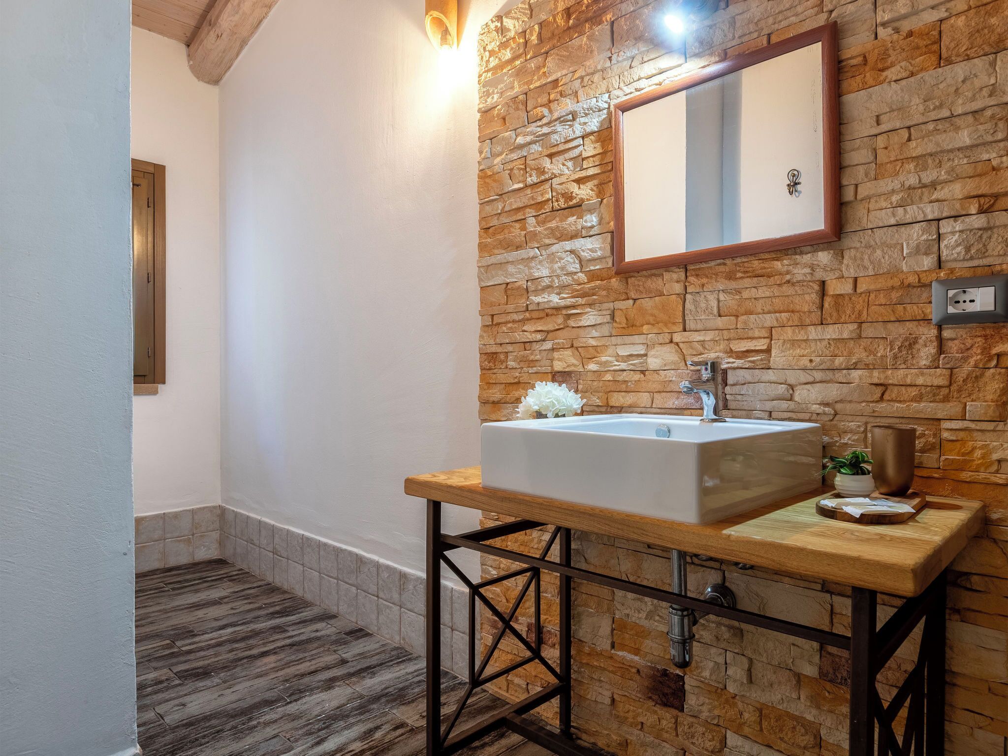 A bathroom with a stone wall, a wooden vanity, a large mirror, and a white sink.