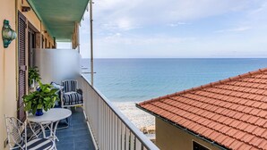 Ein Balkon mit Tisch und Stühlen, der auf einen Strand und das Meer blickt.