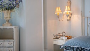 Ein Schlafzimmer mit einem Bett, einem Nachttisch mit Teekanne, einer Lampe und einer Kommode mit Schubladen.