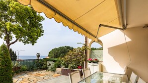 Une terrasse extérieure avec une table et des chaises en verre, un auvent jaune et une vue sur la mer.