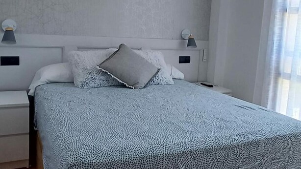 Une chambre à coucher avec un lit, deux tables de chevet, une commode, une lampe et une fenêtre avec des rideaux.