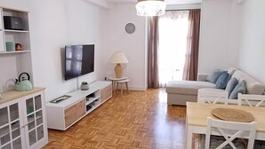 Un salon moderne doté d’un téléviseur à écran plat, d’un canapé blanc, d’une table à manger avec des chaises et d’un parquet en bois à motifs en chevrons.