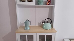 Une petite cuisine équipée d’une machine à café et d’une bouilloire, le tout posé sur un plan de travail en bois, au-dessus d’un meuble blanc doté de portes en verre.