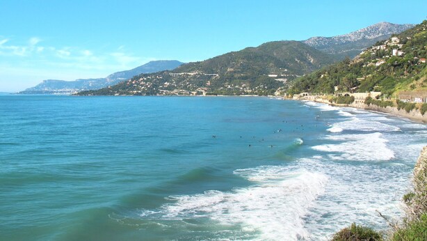 Un paisaje costero con vista despejada al mar, una playa y una colina con edificios.