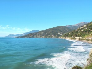 Un paisaje costero con vista despejada al mar, una playa y una colina con edificios.