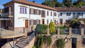Un edificio de dos pisos con fachada blanca, varias ventanas con contraventanas y una escalera de ladrillo que lleva a la entrada.