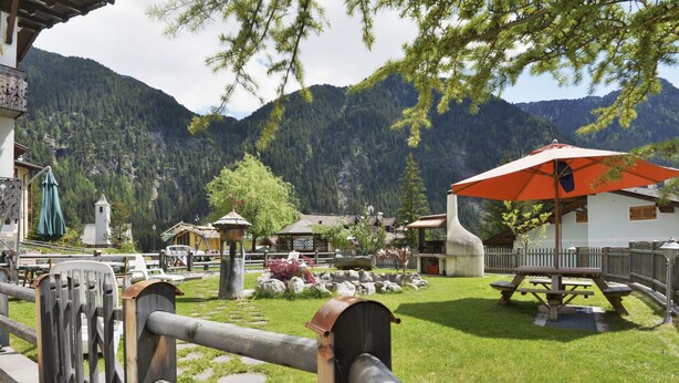 Ein rustikaler Außenbereich mit Holzbänken und einem Picknicktisch, umgeben von einem Holzzaun und Blick auf ein Gebirge.