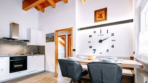 Eine moderne Küche mit Holzbalken, einer großen Wanduhr und einem Essbereich mit zwei Stühlen und einem Tisch.