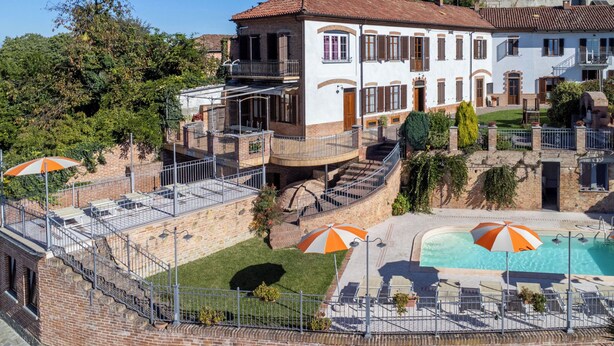 A two-story building with a swimming pool, outdoor seating, and a staircase leading to a balcony.