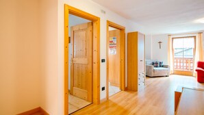 Een ruime woonkamer met houten vloeren, een bank, een rode stoel en een balkon met een hekwerk.