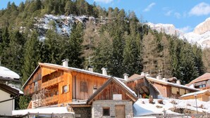 Een houten chalet met een stenen entree, omringd door besneeuwde grond en een bebost berglandschap.