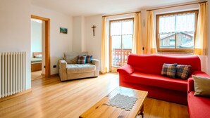 Een woonkamer met een rode bank, een beige fauteuil, een houten salontafel en uitzicht door grote ramen.