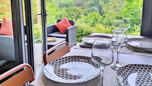Un coin repas avec une table dressée pour quatre personnes, donnant sur un paysage boisé.