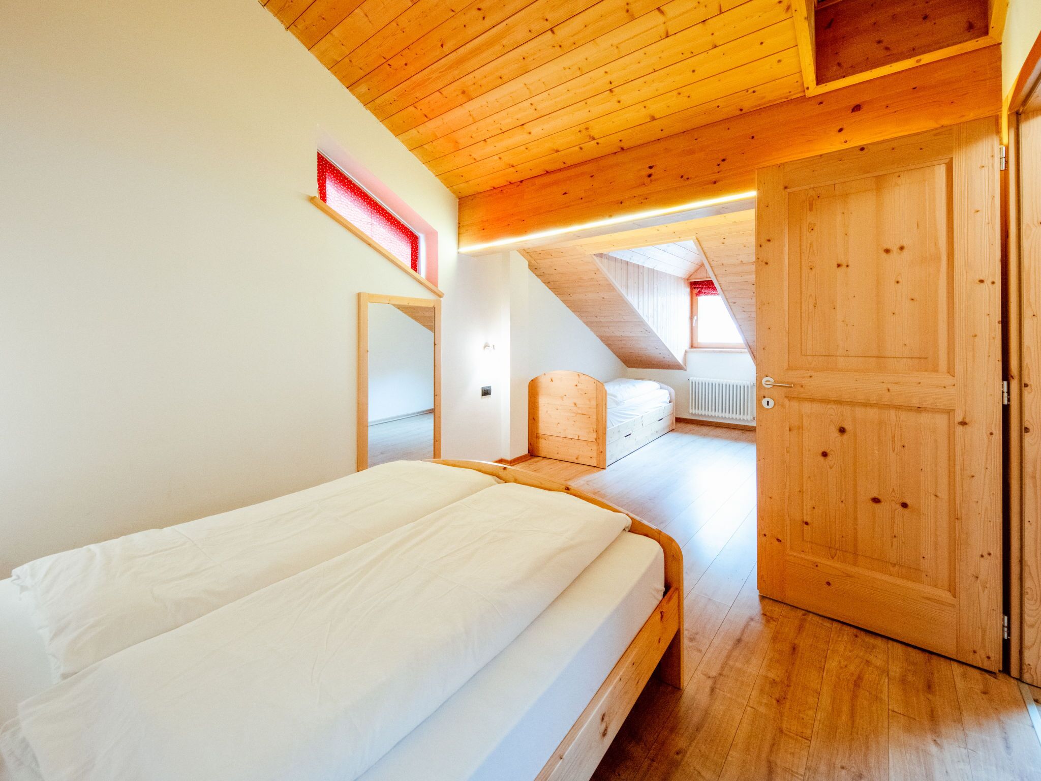A bedroom with a wooden ceiling, a bed, a mirror, and a door.
