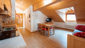 Et hyggeligt, veloplyst køkken med træskabe og en moderne komfur. Et spiseområde med bord og stole er synligt, og et fjernsyn står på et lille bord.