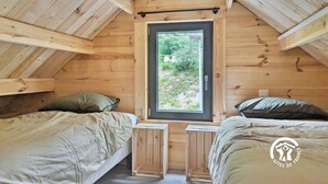 Una cabaña de madera con dos camas, una mesita y un ventanal con vistas a la vegetación.