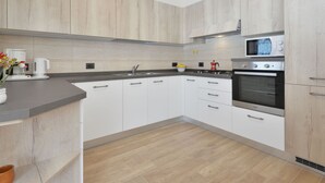 Eine moderne Küche mit hellen Holzschränken, einem Edelstahlbackofen und einer Mikrowelle.