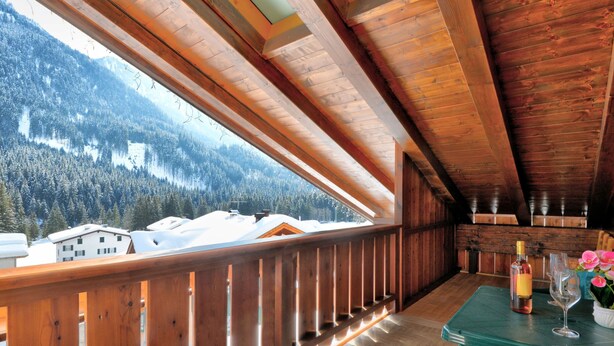 Ein Holzbalkon mit Blick auf schneebedeckte Häuser und einen bewaldeten Berg.