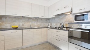 A modern kitchen with light wood cabinets, a stainless steel stove, and a microwave. - Bernard by Interhome (Campitello)