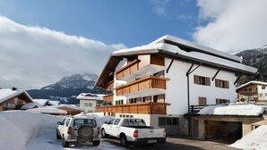 A multi-story building with wooden balconies, a garage, and a snow-covered driveway. - Bernard by Interhome (Campitello)