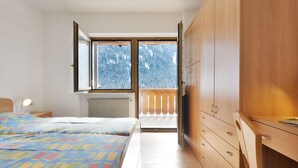 A bedroom with a bed, a dresser, and a window with a view of a snowy landscape. - Bernard by Interhome (Campitello)