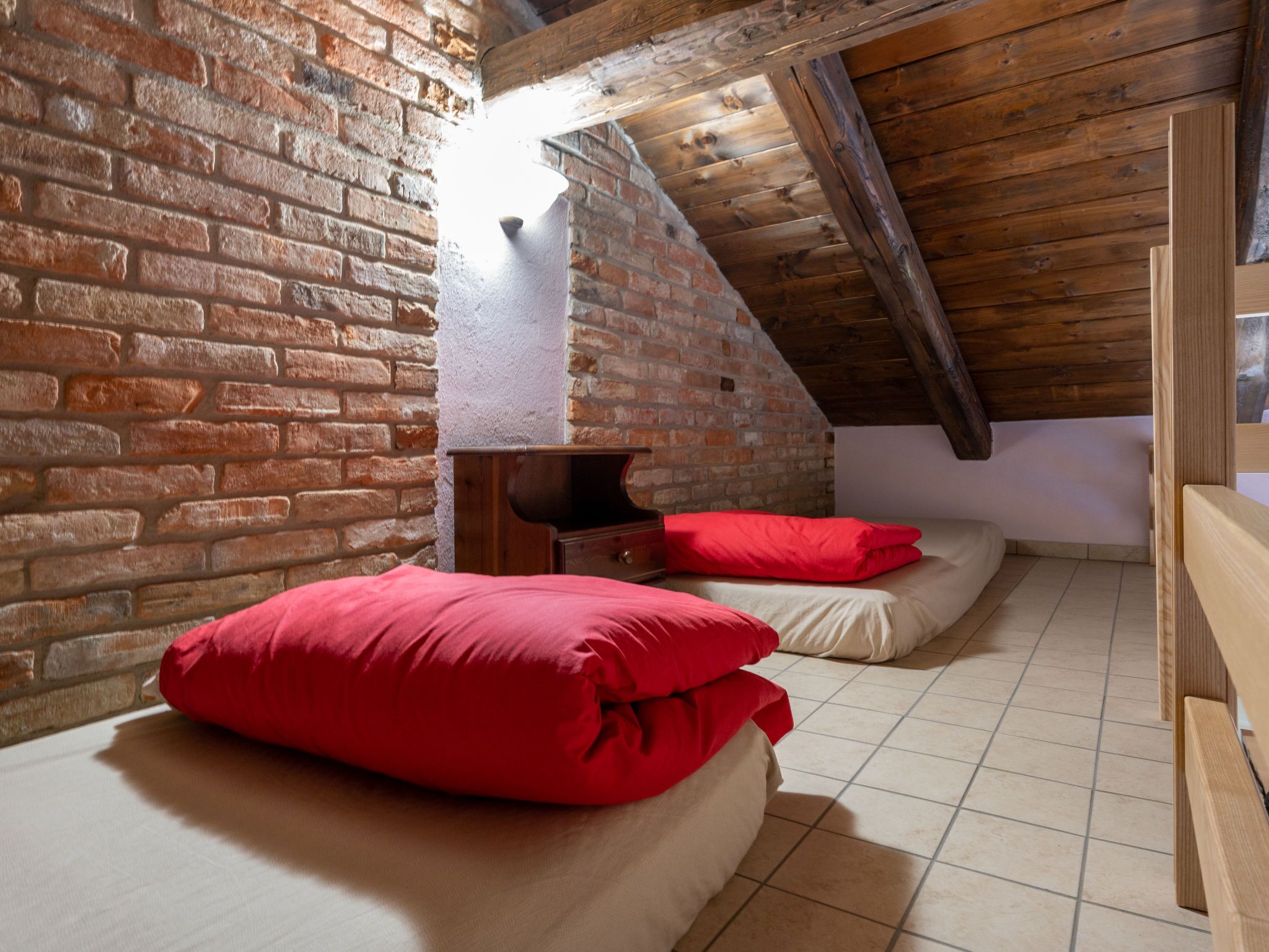 A cozy attic bedroom with exposed wooden beams, a brick wall, and a sloped ceiling.