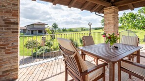 A wooden deck with a table and chairs, overlooking a green landscape with a house in the background.