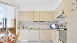 A modern kitchen with light wood cabinets, a stainless steel range, and a tiled backsplash. - Bernard by Interhome (Campitello)