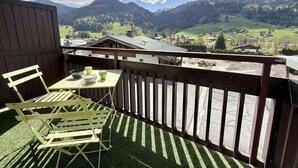 A balcony with a table and chairs, overlooking a mountainous landscape with houses and a construction site. - Cozy 2-Room Cabin Apartment in Praz Sur Arly, Close to Ski Lifts, Sleeps 5, Parking Included (Praz-sur-Arly)
