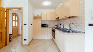 Une cuisine compacte avec des meubles en bois, un four à micro-ondes, un évier et un dosseret carrelé.