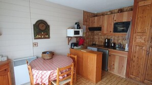 A compact kitchen with a wooden table and chairs, a microwave, a coffee maker, and a dishwasher.