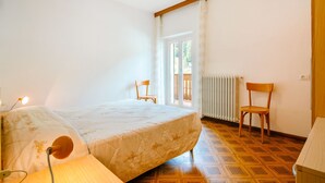 A bedroom with a bed, two chairs, a radiator, and a window with curtains. - Pederiva (SOF740) by Interhome (Soraga di Fassa)