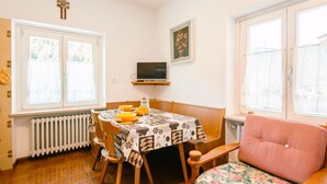 A dining area with a table set for two, a television on a stand, a radiator, and a window with curtains. - Pederiva (SOF740) by Interhome (Soraga di Fassa)