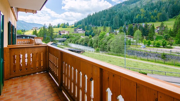 A balcony with a wooden railing overlooking a river, surrounded by greenery and buildings. - Pederiva (SOF740) by Interhome (Soraga di Fassa)