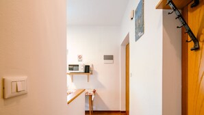 A narrow hallway with a wooden door on the right, a white wall with a no-smoking sign, a small table with a tablecloth, and a microwave on a shelf. - Pederiva (SOF740) by Interhome (Soraga di Fassa)