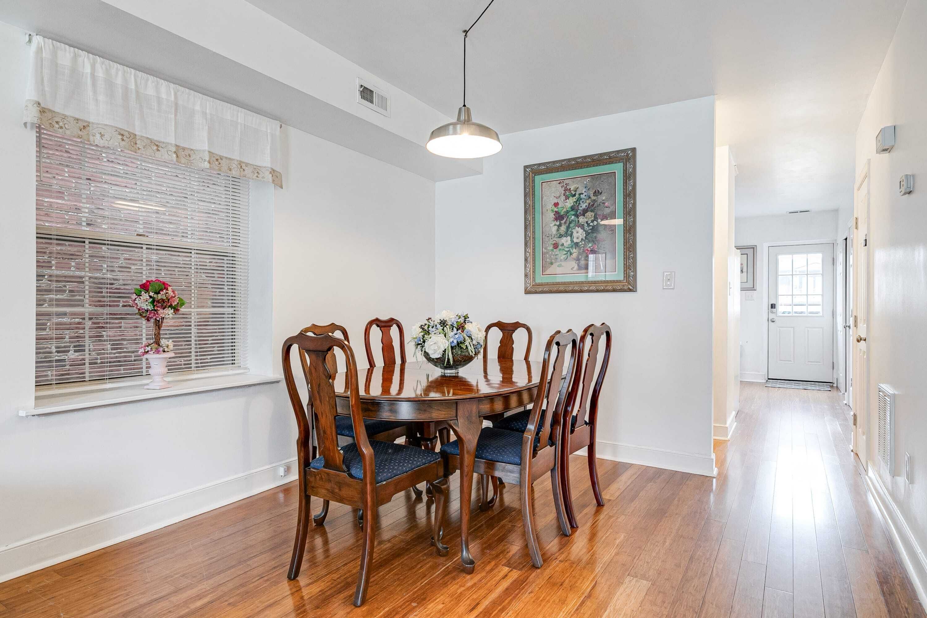 A dining area with a round wooden table, six chairs, and a vase of flowers.