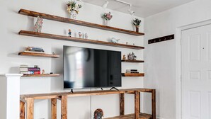 Een woonkamer met een flatscreen televisie bevestigd aan een houten tv-meubel, omringd door planken met decoratieve objecten en boeken.