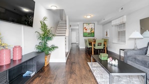 Een moderne woonkamer met een flatscreen televisie, een trap, een eethoek en een grijze bank.