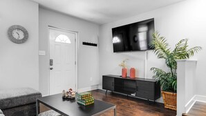 Een moderne woonkamer met een bank, een salontafel, een televisie, een zwart kastje en een potplant.