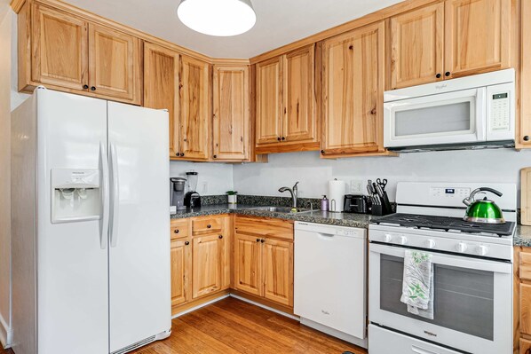 Une cuisine avec des meubles de rangement en bois, un réfrigérateur blanc, un four à micro-ondes, une cuisinière et un lave-vaisselle.