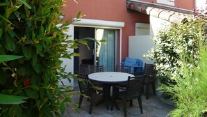 Un patio con una mesa redonda y sillas, una puerta corrediza de vidrio y una pequeña zona cubierta para sentarse.