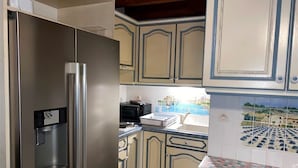 Una cocina con un refrigerador de acero inoxidable, un microondas y una estufa. Los armarios tienen un diseño decorativo con detalles azules y blancos.