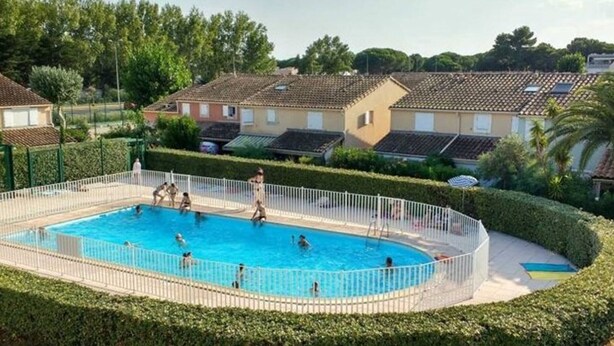 Una piscina rodeada por una cerca blanca, con gente nadando y jugando.