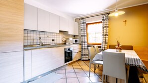 Una cocina moderna con comedor, que presenta suelo de baldosas, armarios de madera, horno integrado y una mesa de comedor con sillas.