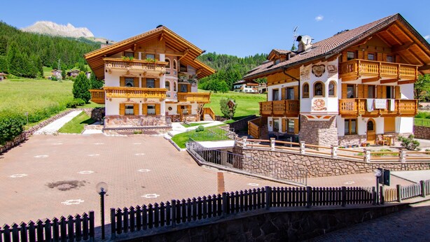 Un hotel de estilo alpino tradicional con varios balcones, fachada de piedra y un patio empedrado.