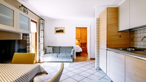 Un espacio habitable compacto con sofá, mesa de comedor, zona de cocina y un dormitorio pequeño con cama y mesita de noche.