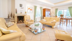 Uma sala de estar ampla com lareira, dois sofás, uma mesa de centro e uma área de jantar com mesa e cadeiras de madeira.