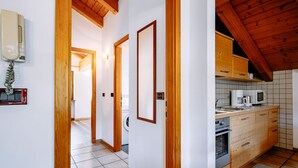 A narrow hallway with wooden door frames and a kitchen area with wooden cabinets and a tiled backsplash. - Apartment Carmen by Interhome (Soraga di Fassa)