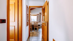 A hallway with wooden doors, a dining area with a table and chairs, and a window with curtains. - Apartment Carmen by Interhome (Soraga di Fassa)